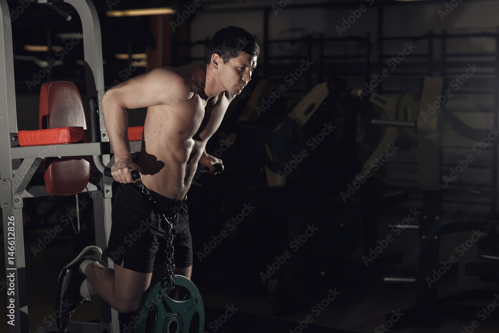Obraz premium Muscular bodybuilder working out in gym doing exercises on parallel bars. Athletic male naked torso.