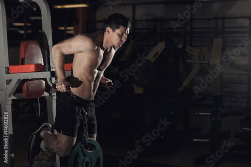 Muscular bodybuilder working out in gym doing exercises on parallel bars. Athletic male naked torso.