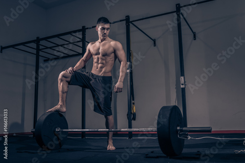 bodybuilder standing on weights bar barbell