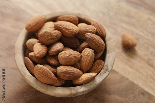 organic almonds in wood bowl on wooden table, shallow focus