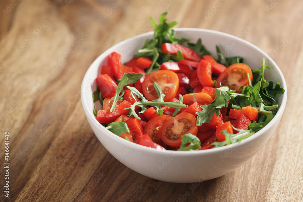 cherry tomatoes with arugula salad in white bowl on wooden table