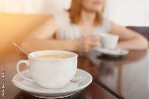 Selective focus on a cup with aromatic coffee. Blurred background with girl drinking coffee cup