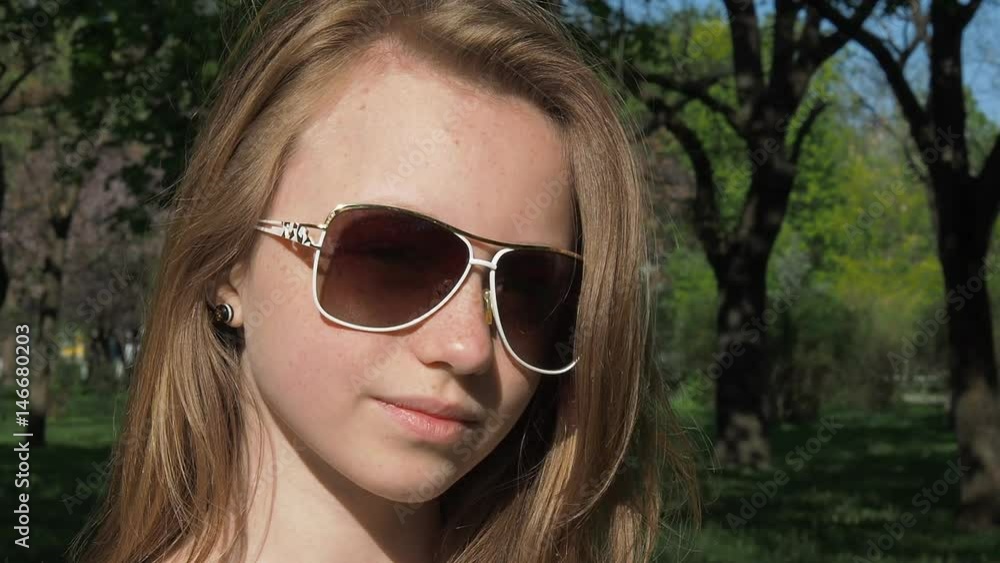 Girl in sunglasses close-up. A teenage girl with freckles takes off glasses in nature. Hands in bracelets. The girl is straightening her hair. Girl in sunglasses close-up. A teenage girl with freckles takes off glasses in nature. Hands in bracelets. The girl is straightening her hair.
