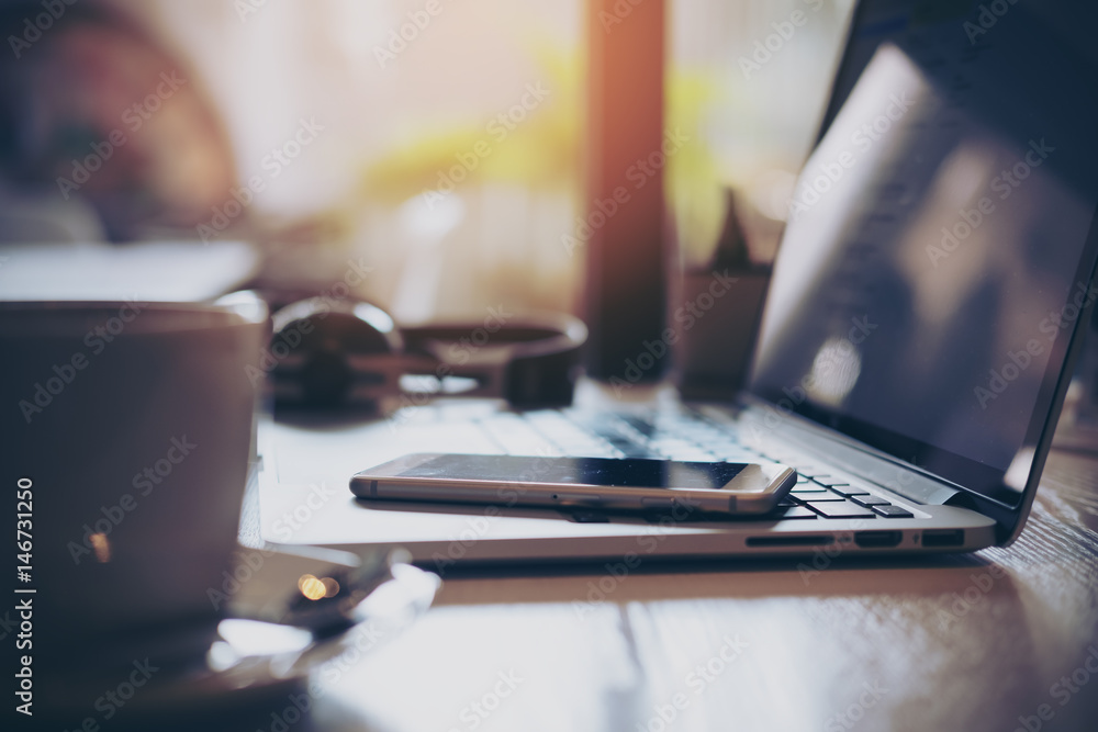 Closeup image of laptop , smart phone , coffee and headphone on wooden table in office Closeup image of laptop , smart phone , coffee and headphone on wooden table in office