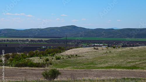 The view of a mountainside overgrown with fruit trees and shrubs in the background of plowed fields in a valley among the beautiful Balkan mountains in spring, near from Aytos Bulgaria.