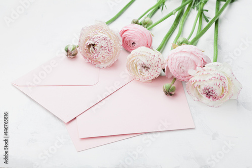 Fototapeta Naklejka Na Ścianę i Meble -  Envelope or letter, paper card and pink ranunculus flowers on white table for greeting on Mother or Woman Day. Can be used as wedding mockup.
