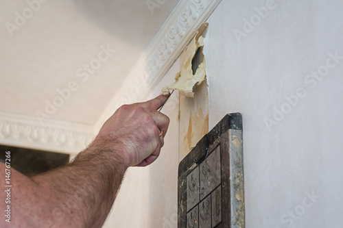 Removing the old wallpaper of the wall by using a steam device and filling knife