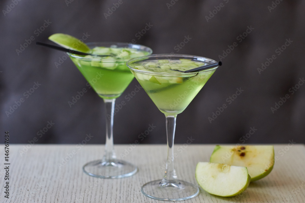 Two glasses of apple martini and apple slices on table in cafe Two glasses of apple martini and apple slices on table in cafe