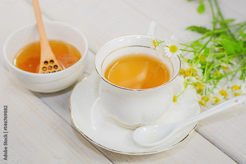 Bowl filled with flower honey and spoon with a cup of tea Bowl filled with flower honey and spoon with a cup of tea