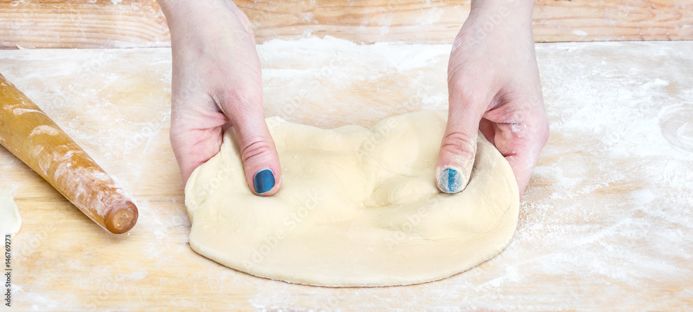 Female hands kneads raw dough.