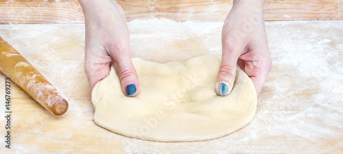 Female hands kneads raw dough.