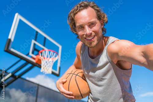 Basketball player man taking fun selfie photo at court net with basket ball. © Maridav