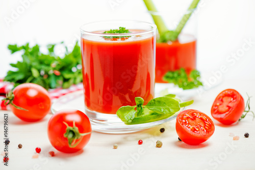 tomato juice in glasses with greenery, basil, cutted tomato fruit and napkin on light wooden background, concept vegetarian food, close up