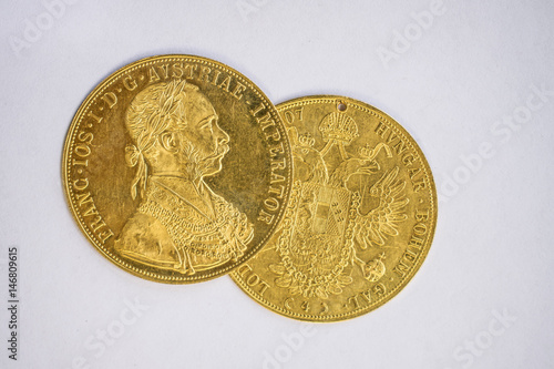 Close-up view of two on one another Austria-Hungary thalers, avers and revers of golden coin-ducats from 1915 with Kaiser Franz Joseph I, on white background