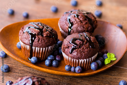 Chocolate muffins with chocolate syrup, blueberries and mint in a wooden background