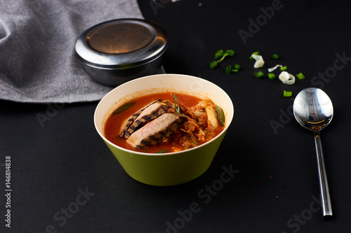 Korean cuisine. Spicy kimchi soup served in a bowl standing on black background.