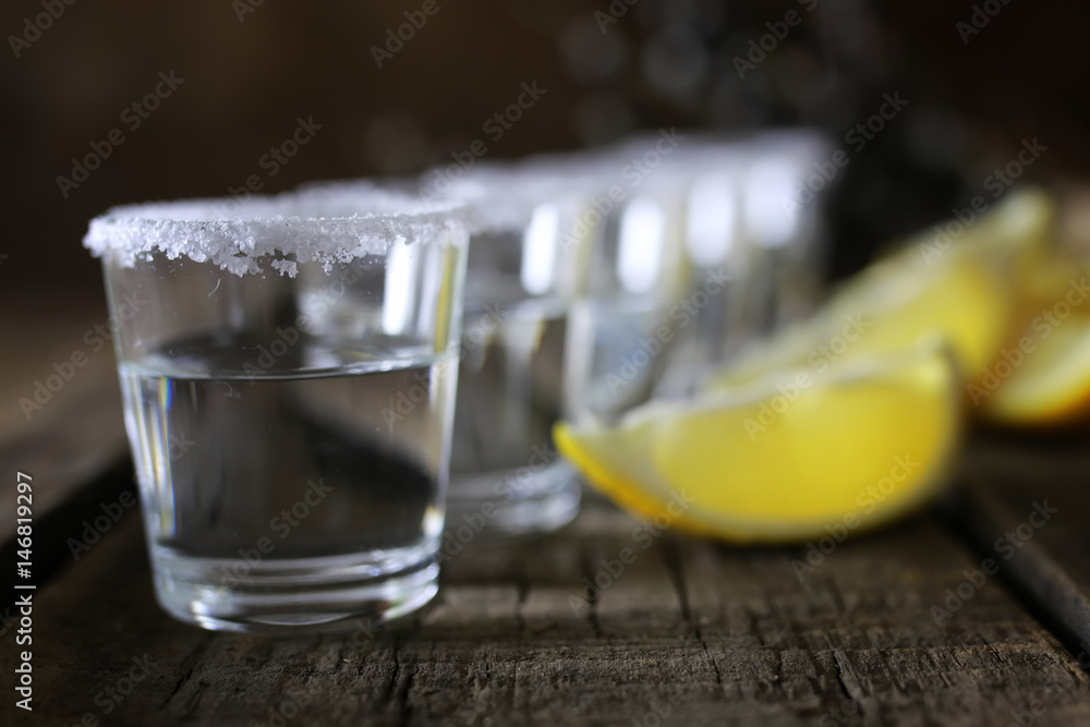 stack of tequila with salt and lemon on a wooden background