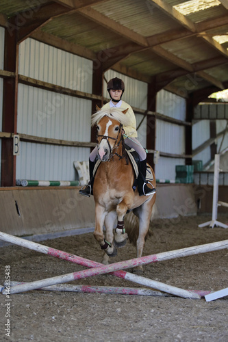 jeune fille adolescente sautant obstacle avec son cheval dans manège