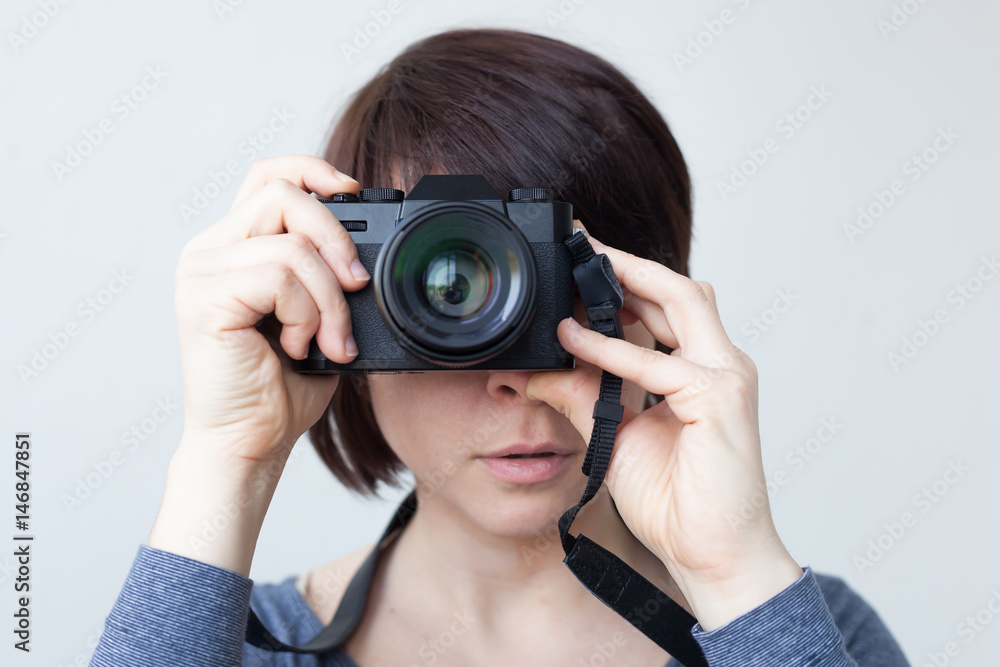 A girl is holding a camera by her face. The lens looks like a big eye. Hobby with photography A girl is holding a camera by her face. The lens looks like a big eye. Hobby with photography