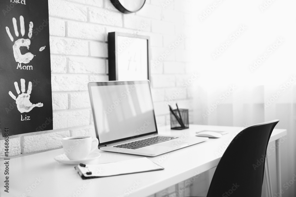 Fototapeta premium Modern home office workspace with laptop, coffee, and family handprints on white brick wall