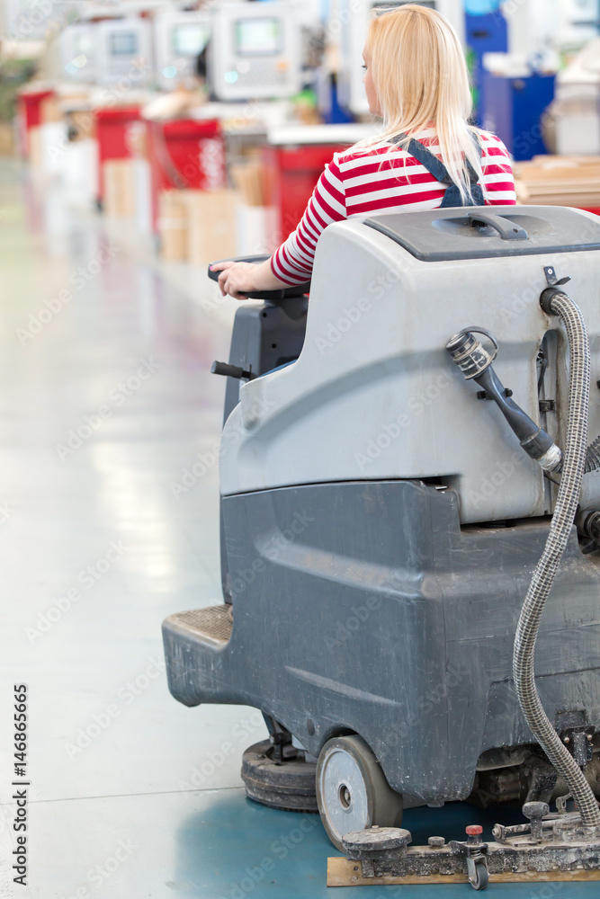 Fototapeta premium Woman Worker Cleaning Factory Workshop Floor with Washing Vacuum Cleaner