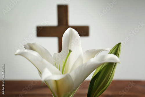 White lily and blurred wooden cross on background