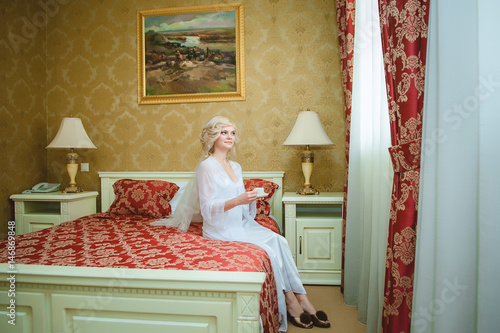 Красивая блондинка невеста утром в спальне пьет кофе
