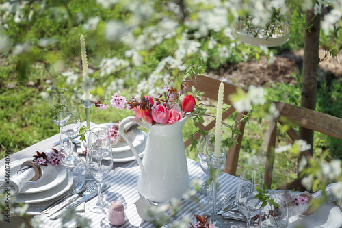 Jug with blooming bouquet of flowers on served table in garden