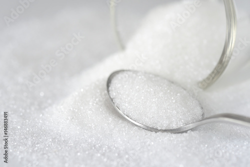 Spoon with white granulated sugar on white texture background. Unhealthy food concept.