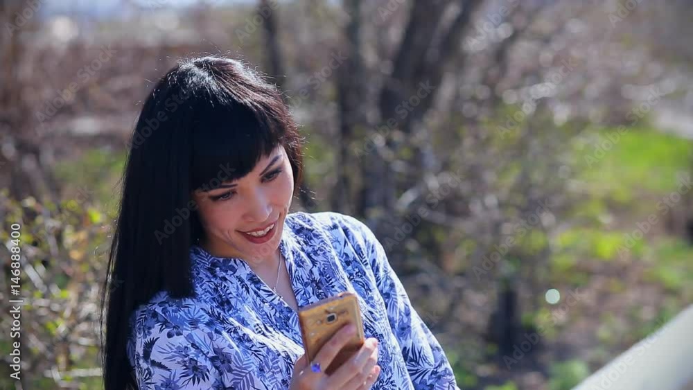 Beautiful asian girl sits in a park on a bench and writes a message on a smartphone Beautiful asian girl sits in a park on a bench and writes a message on a smartphone