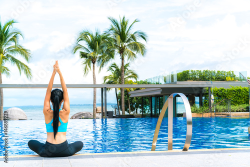 Portrait of young woman (fitness, yoga, perfect tanned body, healthy skin) at luxury swimming pool. Travel and Vacation. Freedom Concept. Outdoor shot.