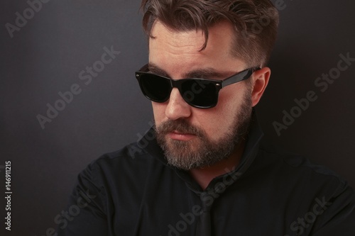 A brutal man with a beard and a stylish hairdo in a black suit and sunglasses