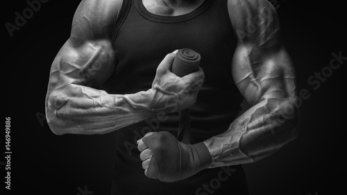 Strong hands and fist, ready for training and active exercise Close-up photo of strong man wrap hands Man is wrapping hands with boxing wraps isolated on black background © USM Photography