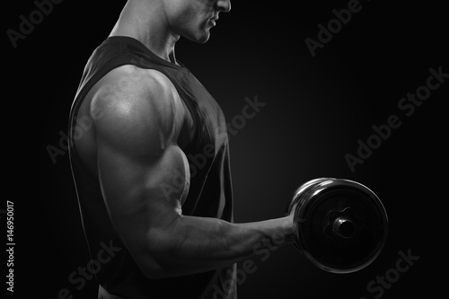 Close-up photo of handsome power athletic man in training pumping up muscles with dumbbell. Strong bodybuilder with perfect deltoid muscles, shoulders, biceps, triceps and chest