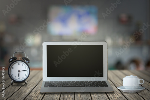 Laptop with retro alarm clock and coffee cup on the wood table over the coffee shop blurred background