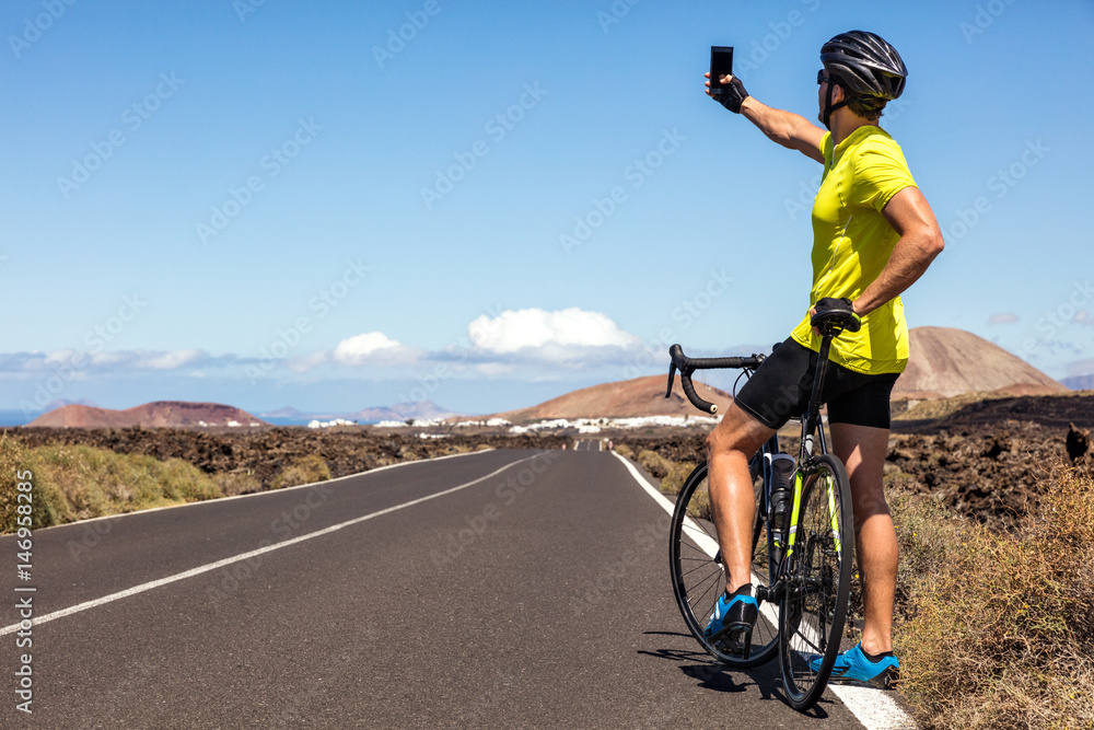 Fototapeta premium Cyclist tourist taking selfie picture with smartphone during biking trip alone on summer vacation travel. Man riding road bike using phone to take photos during holidays.