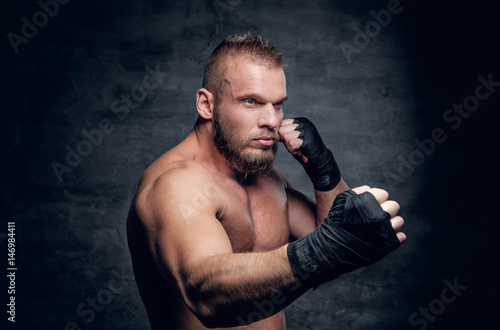 Studio portrait of brutal bearded fighter over dark grey background.