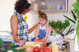 Attractive brunette female with curly hair and her cute little daughter cooking food in a home kitchen.