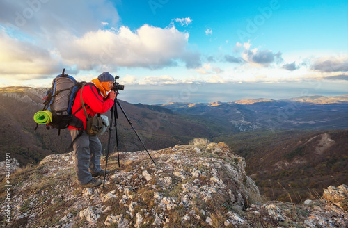 Photographer takes pictures on top of the mountain in autumn. Traveler with backpack enjoying a view from the mountain top