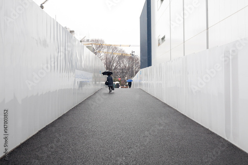 Narrow straight pedestrian sidewalk between the metal white walls