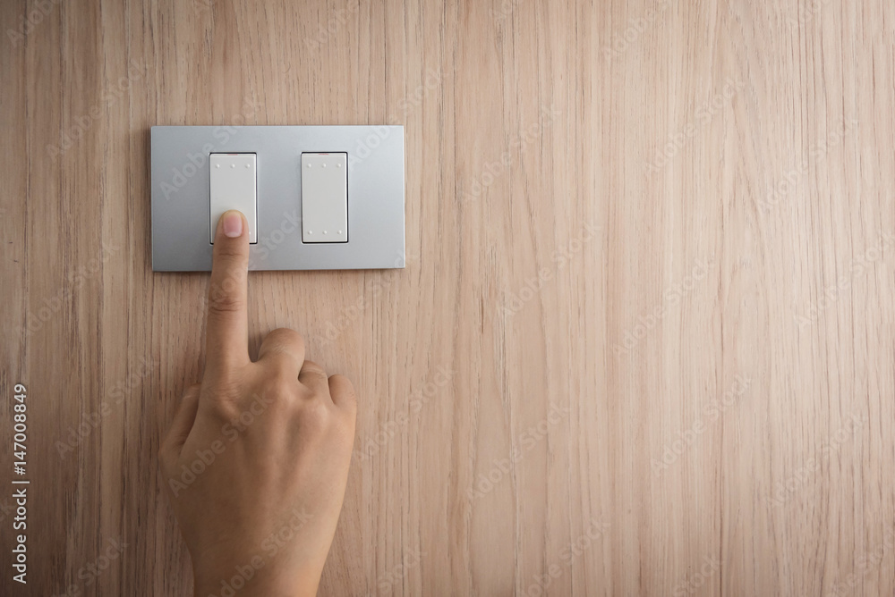 Close up hand turning on or off on grey light switch with wooden background. Copy space. Close up hand turning on or off on grey light switch with wooden background. Copy space.