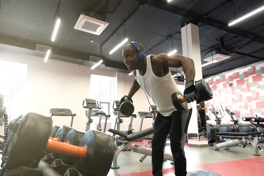 Muscular black man doing exercises with dumbbells at gym Muscular black man doing exercises with dumbbells at gym