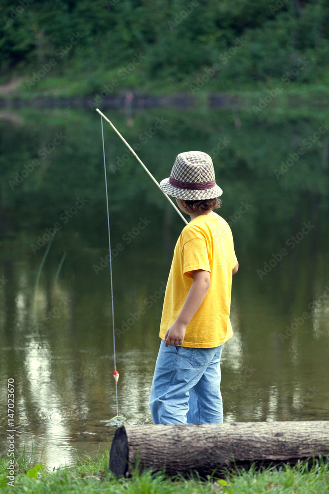 Happy boy go fishing on the river, one children fisherman with a fishing rod on the shore of lake Happy boy go fishing on the river, one children fisherman with a fishing rod on the shore of lake