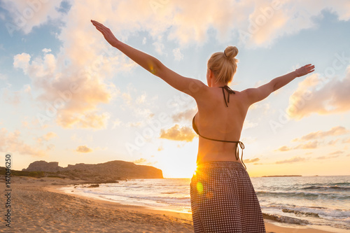 Relaxed woman enjoying sun, freedom and life an beautiful beach in sunset. Young lady feeling free, relaxed and happy. Concept of vacations, freedom, happiness, enjoyment and well being. photo