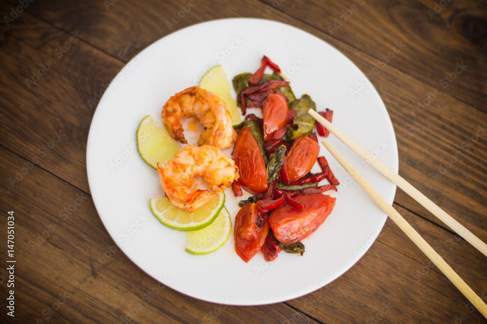 King prawn dish with lime and spinach with tomato and pepper. Wooden background. Top view. Close-up King prawn dish with lime and spinach with tomato and pepper. Wooden background. Top view. Close-up
