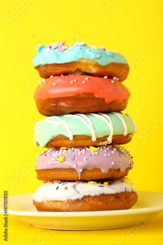 Tasty donuts with sprinkles in plate on yellow background