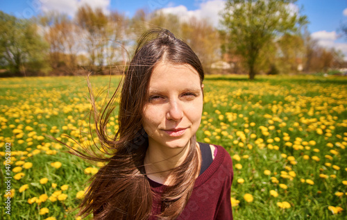 Beautiful young woman relaxing on a meadow with many dandelions in the spring sun. Portrait shot with windy  breezily hair - smiling.