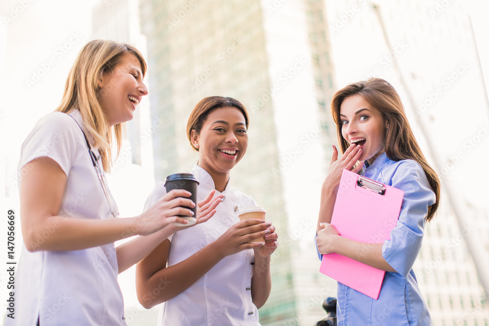 Two nurses and one doctor stand together and smile in time of coffee break, outdoors