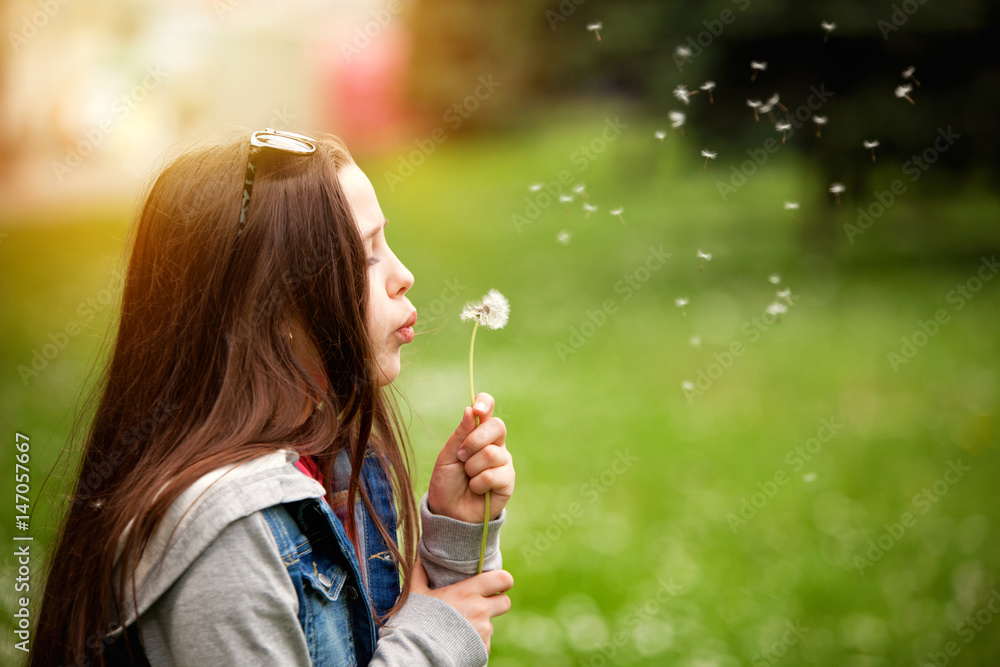 Cute teenage girl in the summer garden blowing a dandelion