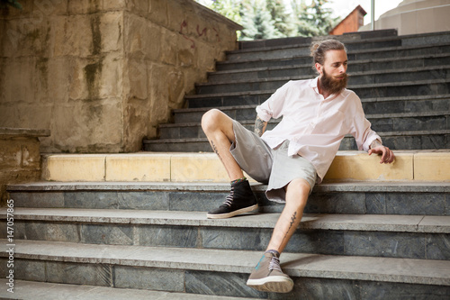 Fashion tattoed and bearded guy posing outdoor in the city